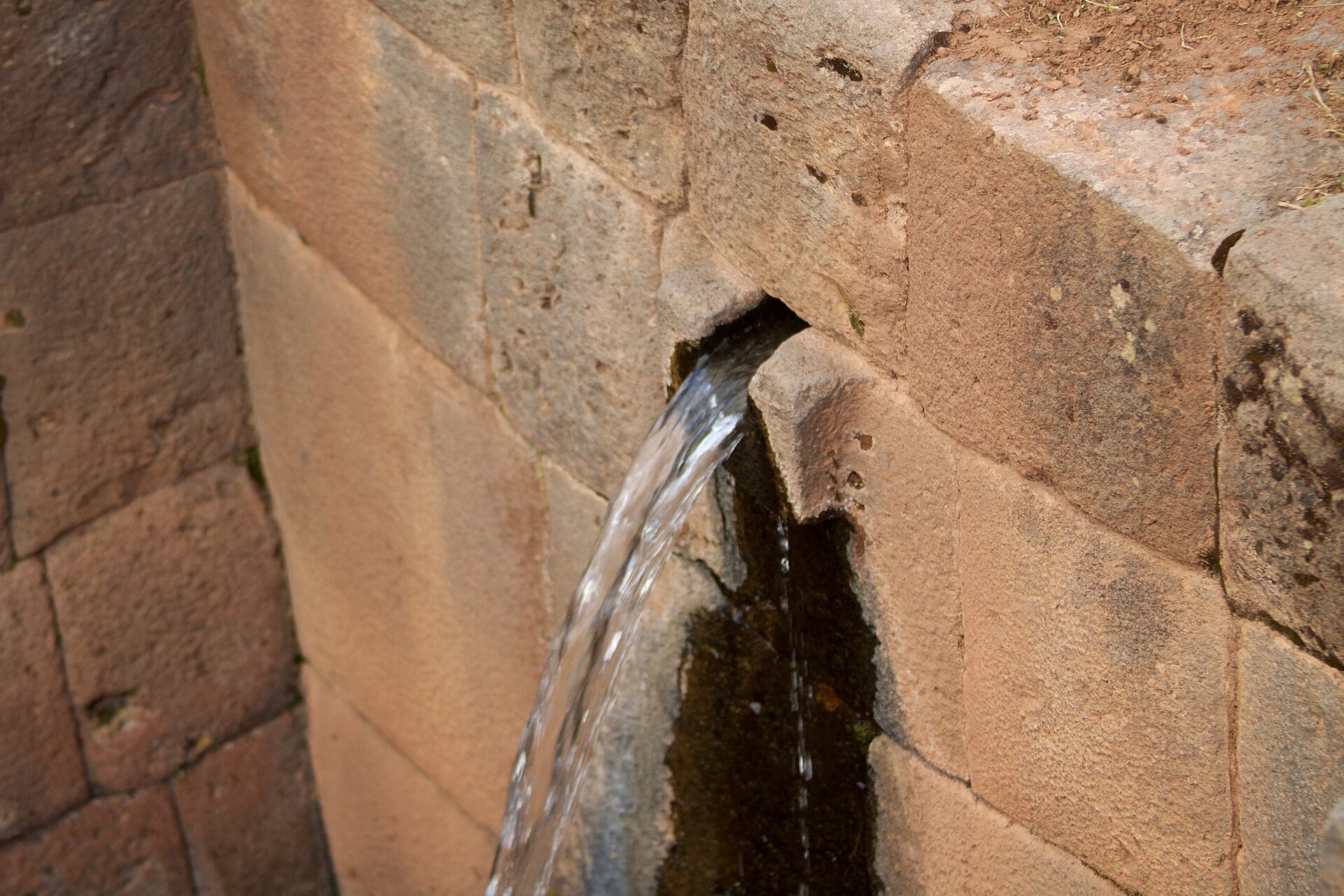 Water pouring from a carved stone spout set in a wall of fitted Inca stone blocks