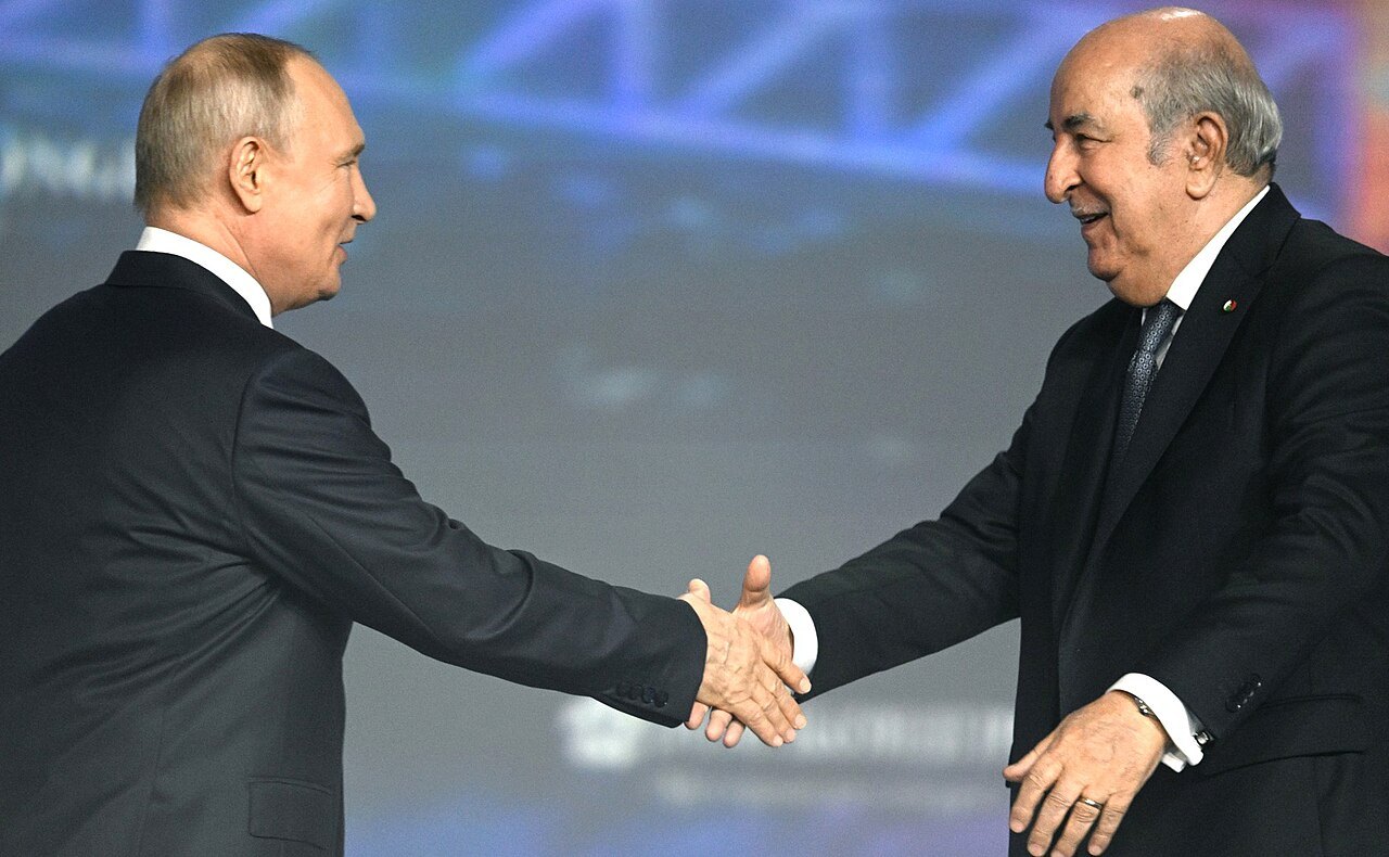 Vladimir Putin and Abdelmadjid Tebboune shaking hands on a conference stage