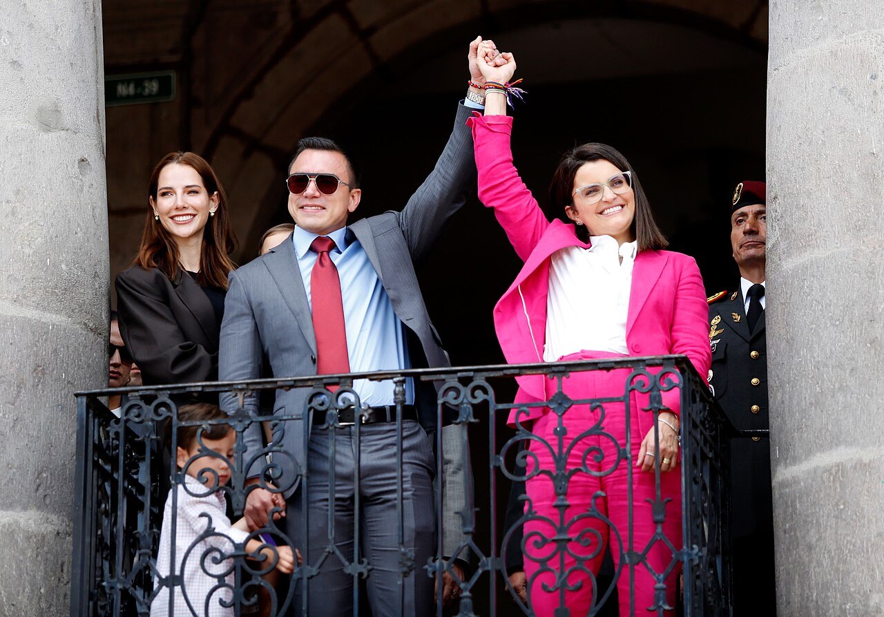 Daniel Noboa and María José Pinto raise joined hands on a balcony of Carondelet Palace in Quito, with Lavinia Valbonesi beside them