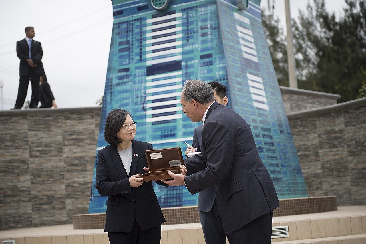 Asfura bows slightly as he hands a wooden box holding a city key to Taiwan's president Tsai Ing-wen outdoors