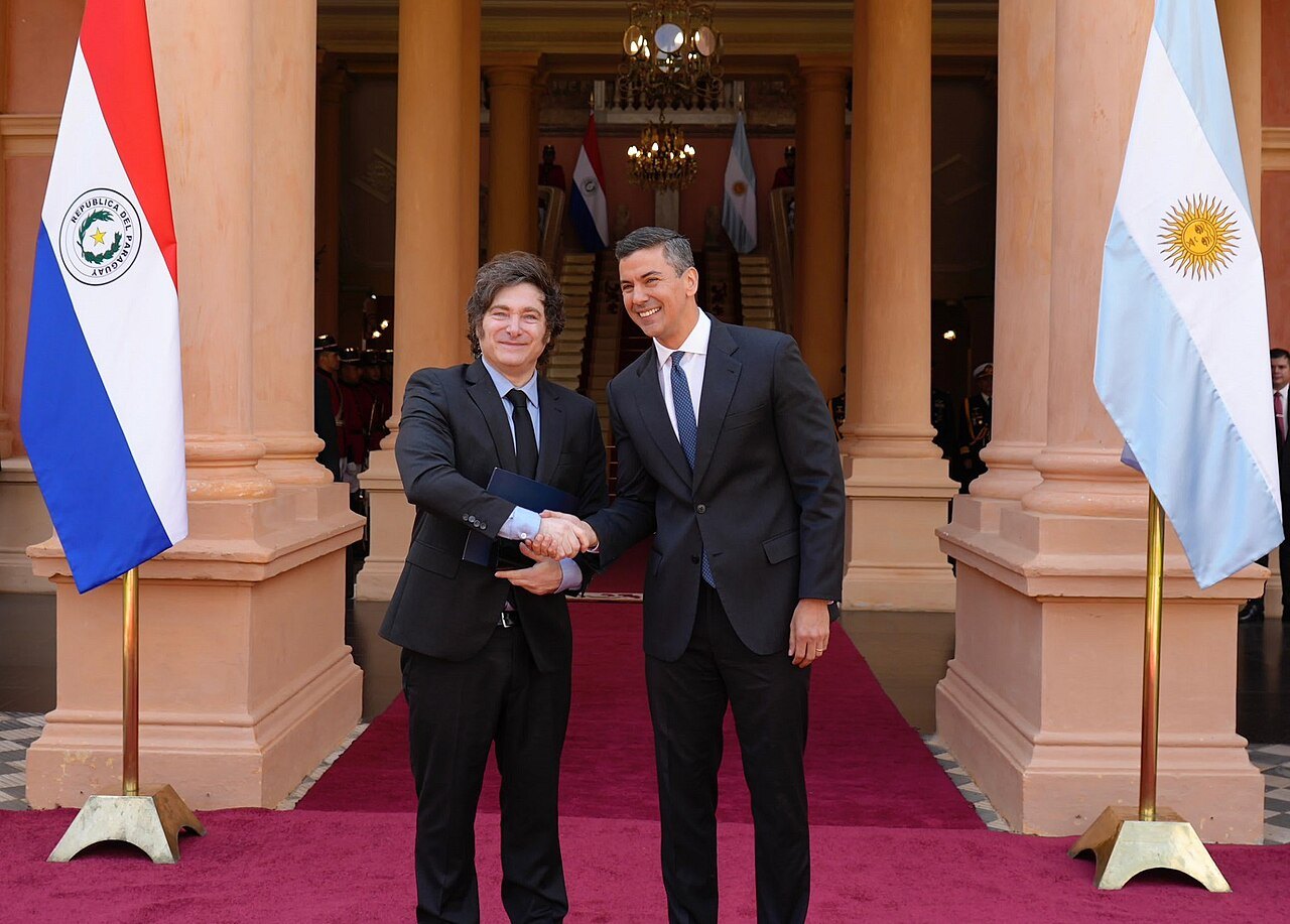 Javier Milei and Santiago Peña shaking hands between the flags of Argentina and Paraguay