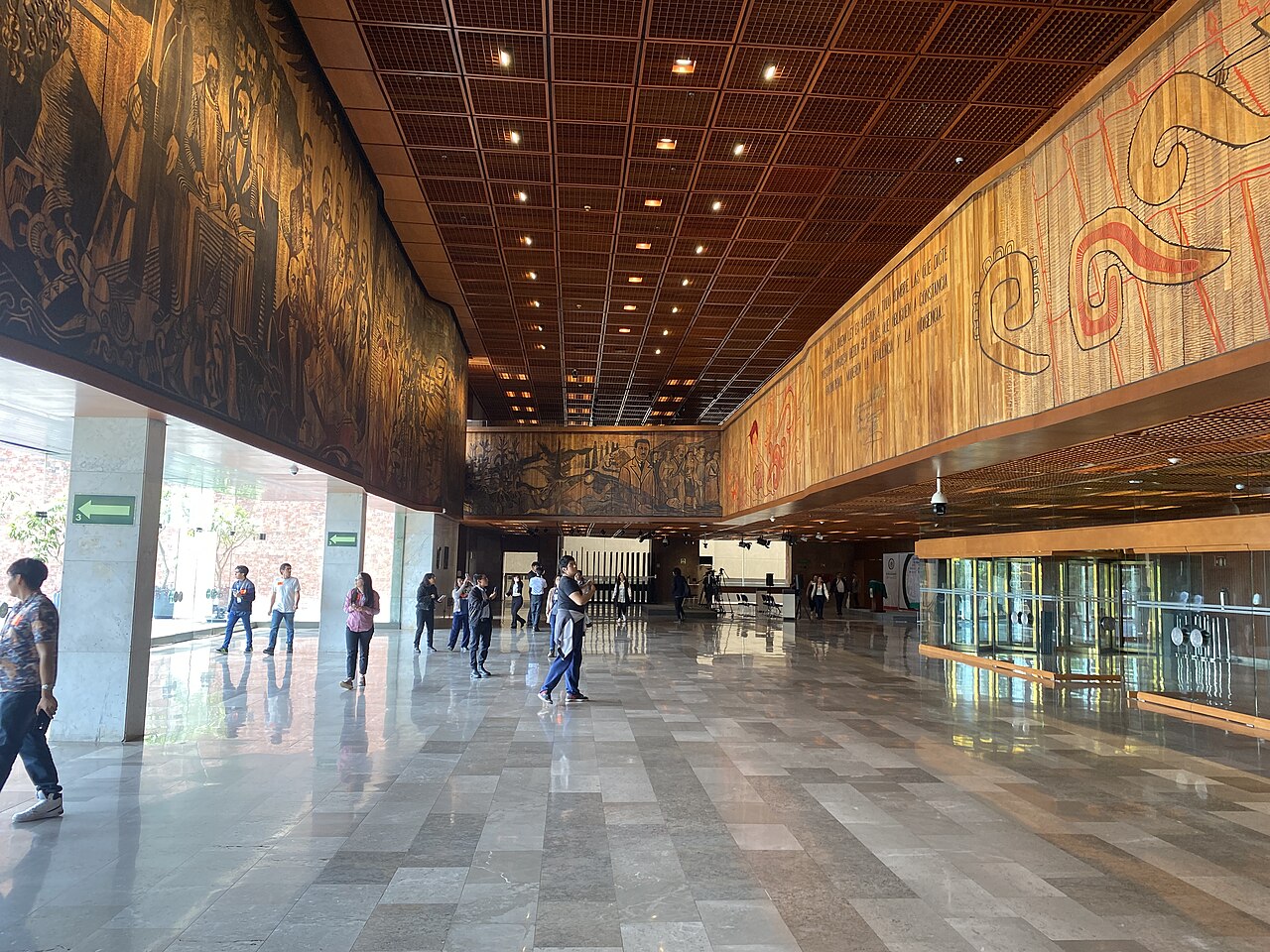 Visitors walk through the marble lobby of the Legislative Palace of San Lázaro under large wall murals