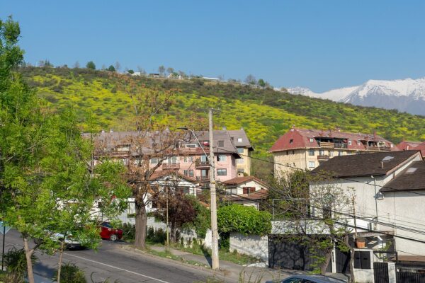 Houses and apartment blocks on a hillside street below Cerro Apoquindo in Las Condes, with snow-capped Andes peaks behind