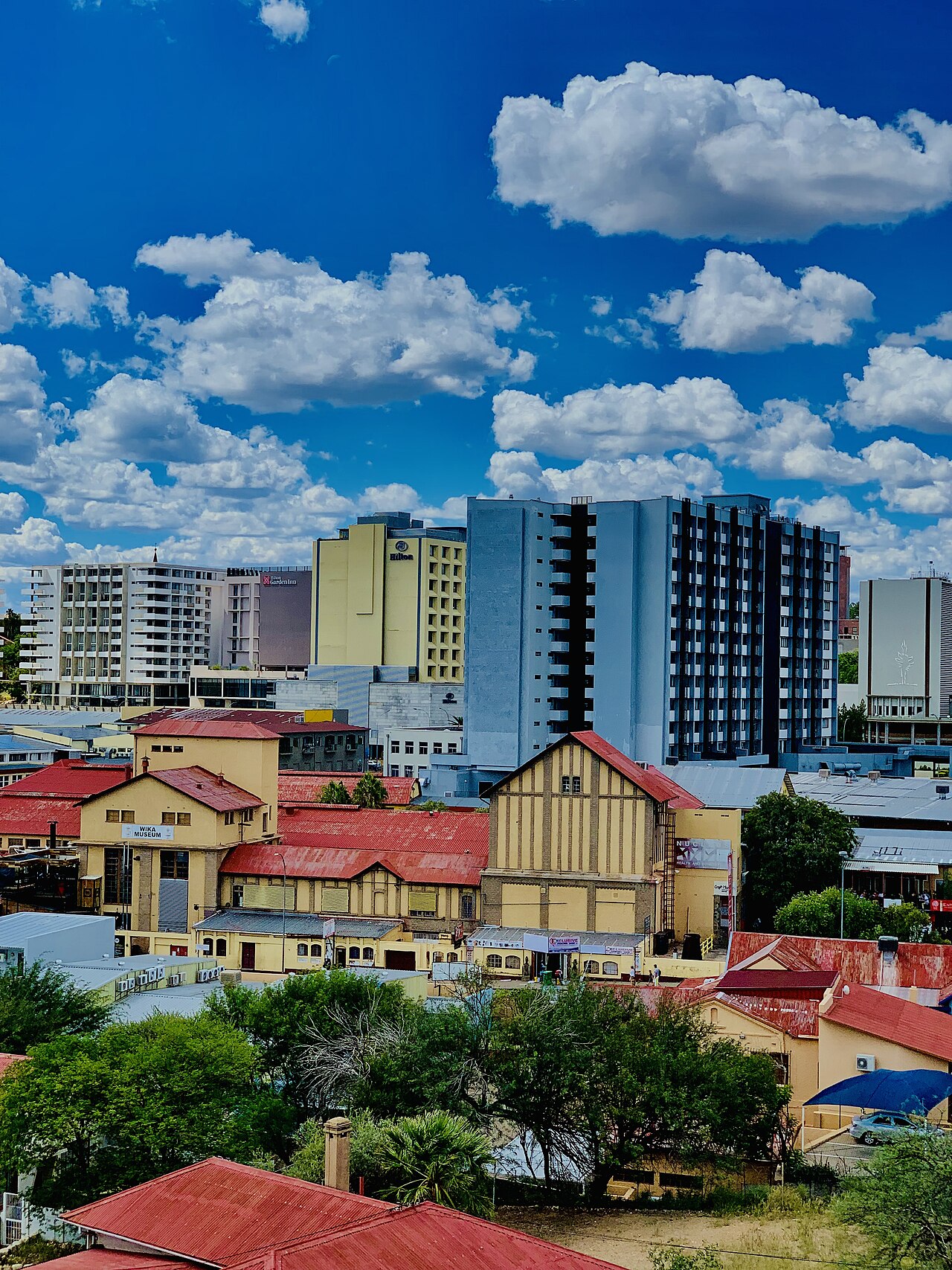 Hotel and apartment towers rise behind the red-roofed Wika Museum buildings in central Windhoek under a blue sky