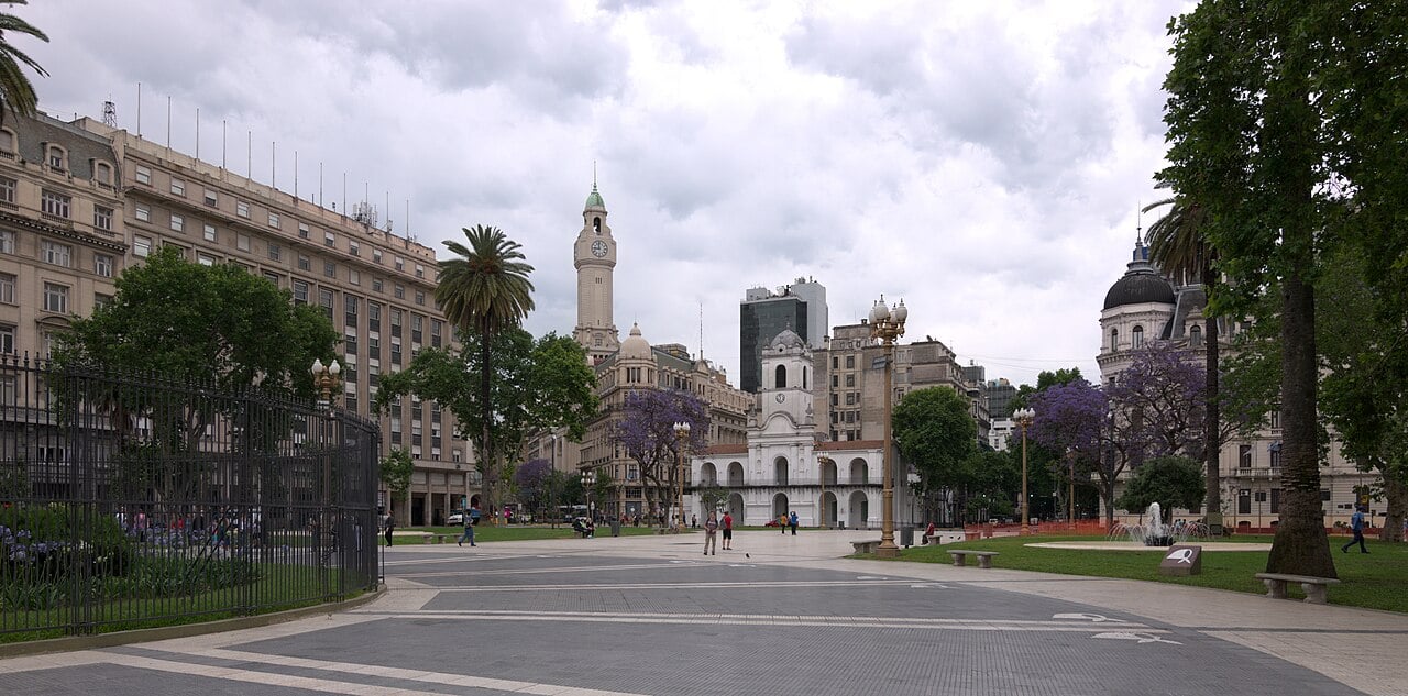 Plaza de Mayo in Buenos Aires with the white colonial Cabildo building at centre, office buildings on the left and jacaranda trees in bloom