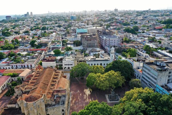 Aerial view of Santo Domingo's Colonial City with a church roof, a tree-filled plaza and the city skyline behind