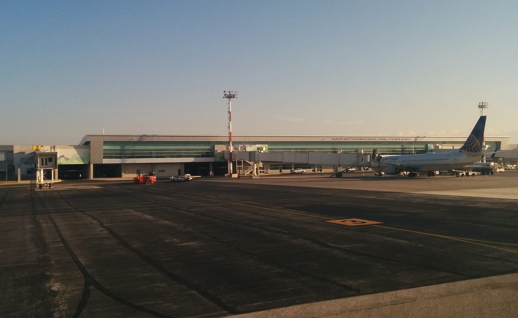 Daniel Oduber Quiros International Airport terminal in Liberia, Costa Rica, seen from the apron, with a United Airlines jet parked at a jet bridge in low evening light