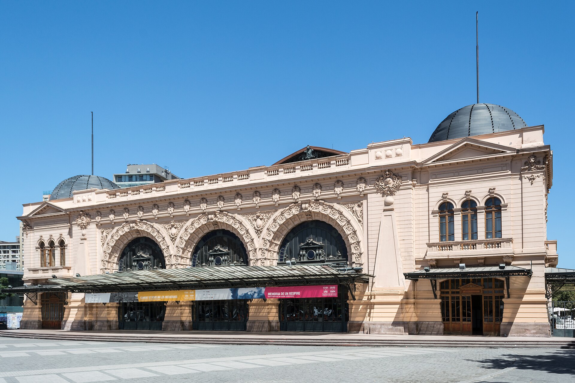 The cream facade of the Centro Cultural Estación Mapocho in Santiago with arched windows, two domes and a glass canopy over the entrance, under a clear blue sky