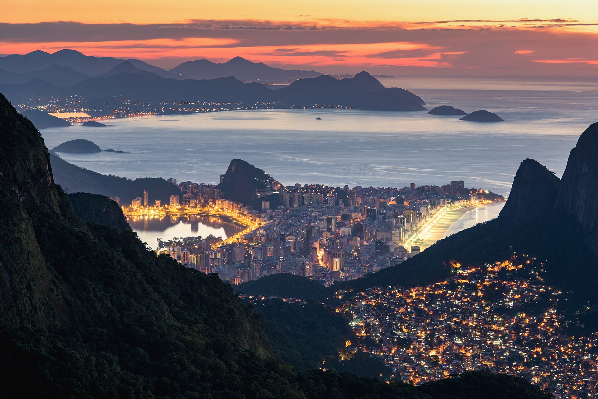 Dawn view from a mountain over Rio de Janeiro: the lit-up hillside favela of Rocinha in the foreground, with the lagoon, the beachfront districts and the Atlantic behind