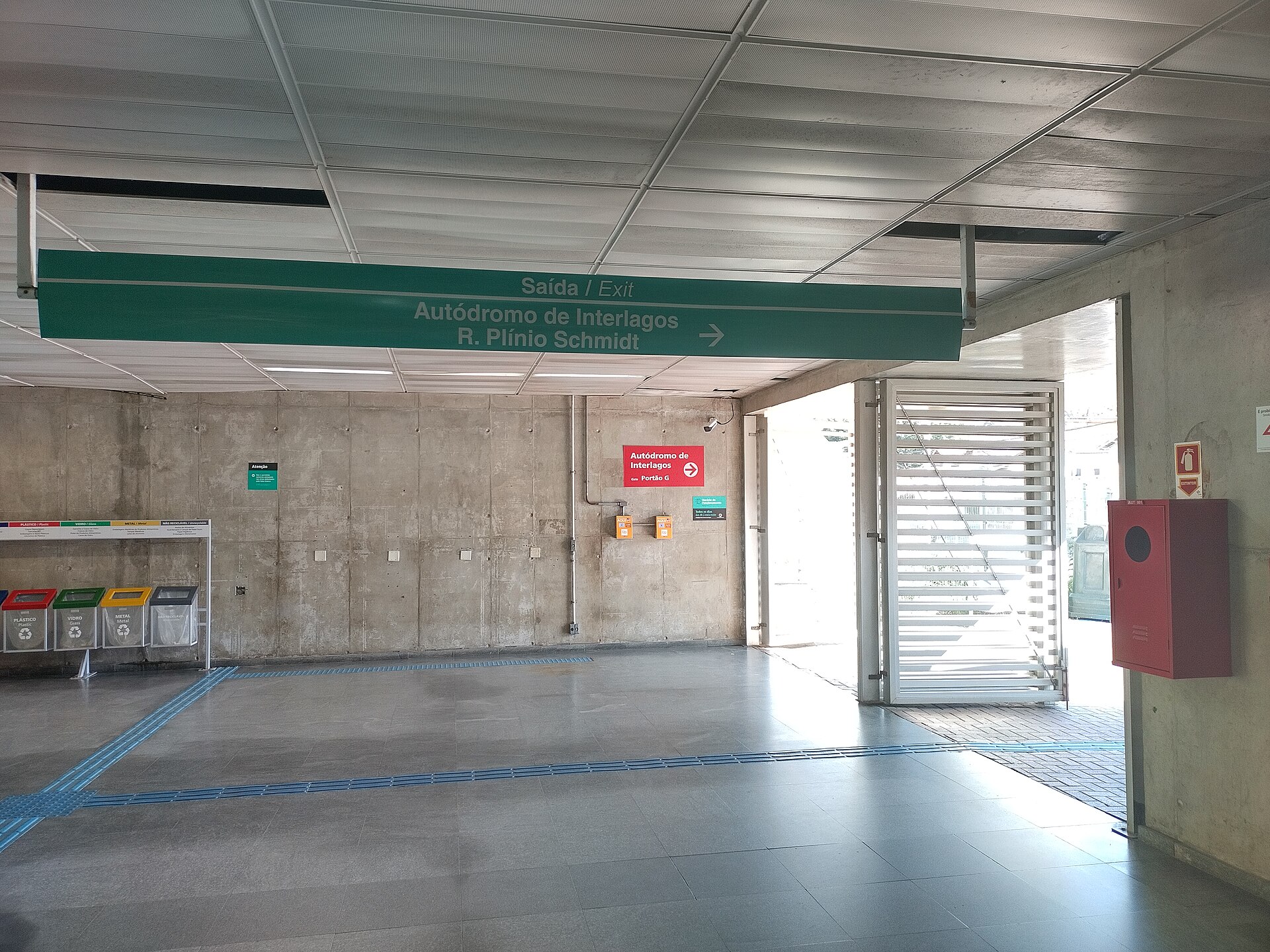 A green sign inside a train station hall reads Exit, Autódromo de Interlagos, R. Plínio Schmidt, with an arrow pointing right
