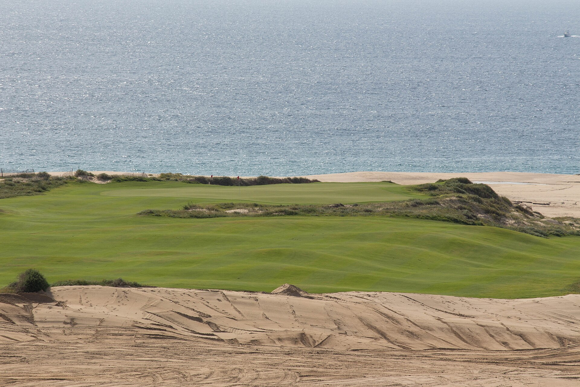 A green fairway and putting green framed by sand dunes, with the Pacific Ocean behind