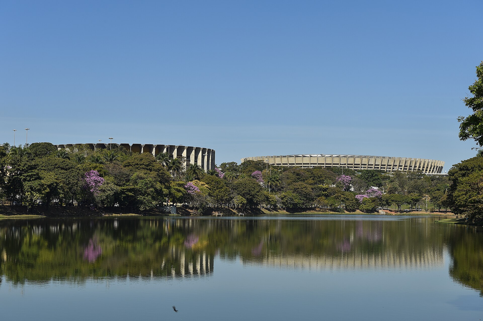 The Pampulha lagoon in Belo Horizonte with the Mineirinho arena on the left and the Mineirão stadium on the right, reflected in the water under a blue sky