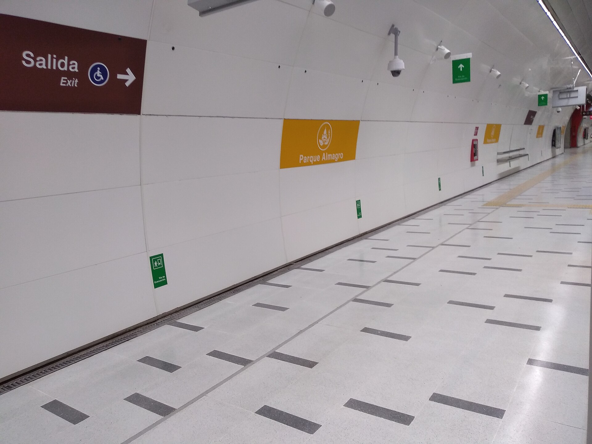 An empty white Metro platform with a yellow Parque Almagro station sign on the curved wall and a brown exit sign