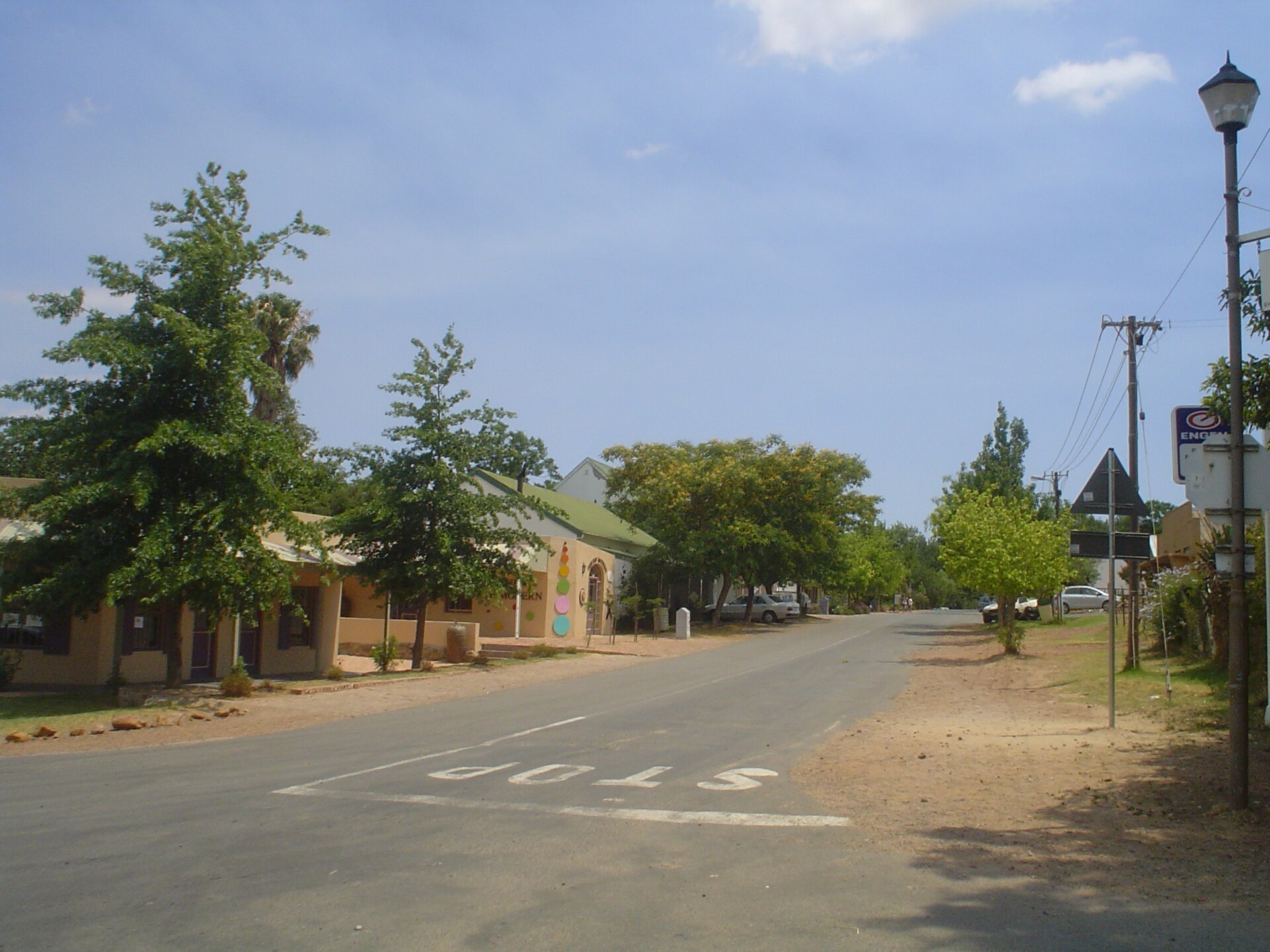 A quiet street at the five way stop in the centre of Greyton, with low shops, green trees and a stop sign road marking