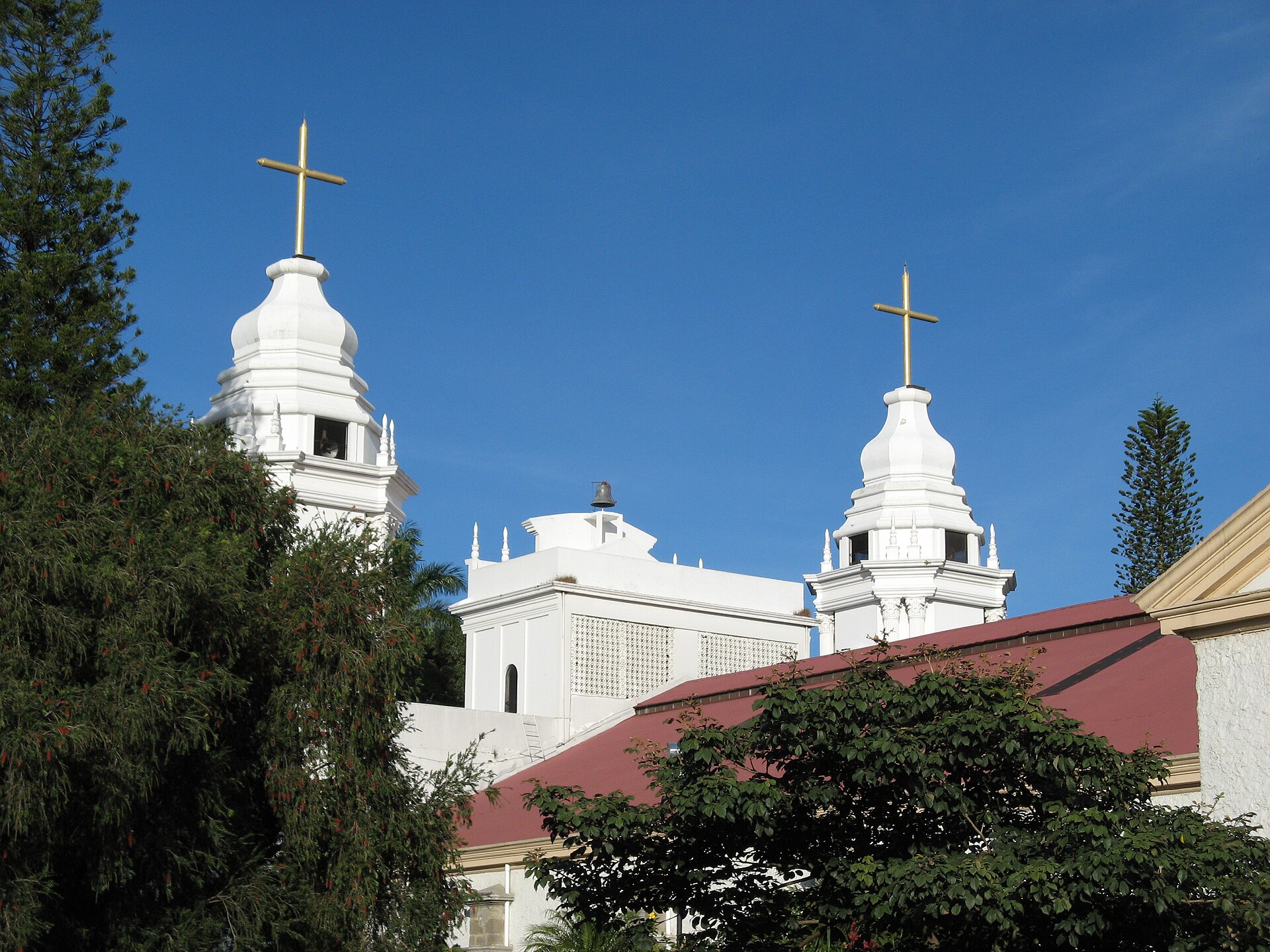 White bell towers topped with gold crosses on a church in Alajuela, Costa Rica, against a clear blue sky