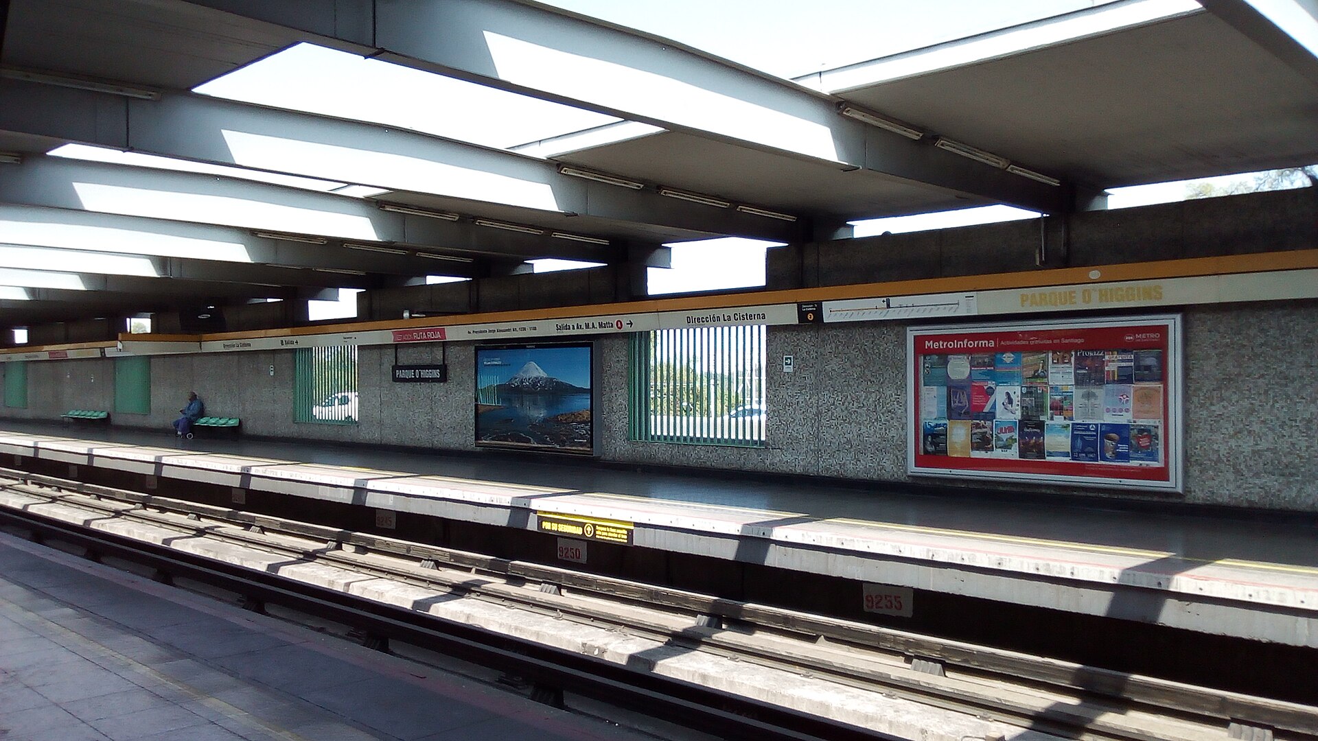 Platforms of Parque O'Higgins Metro station in Santiago under a concrete roof with wall posters and the station name sign