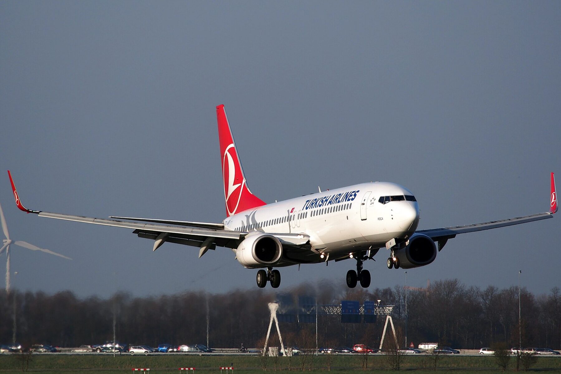 A white Turkish Airlines Boeing 737 with a red tail flares to land over a runway under a grey sky