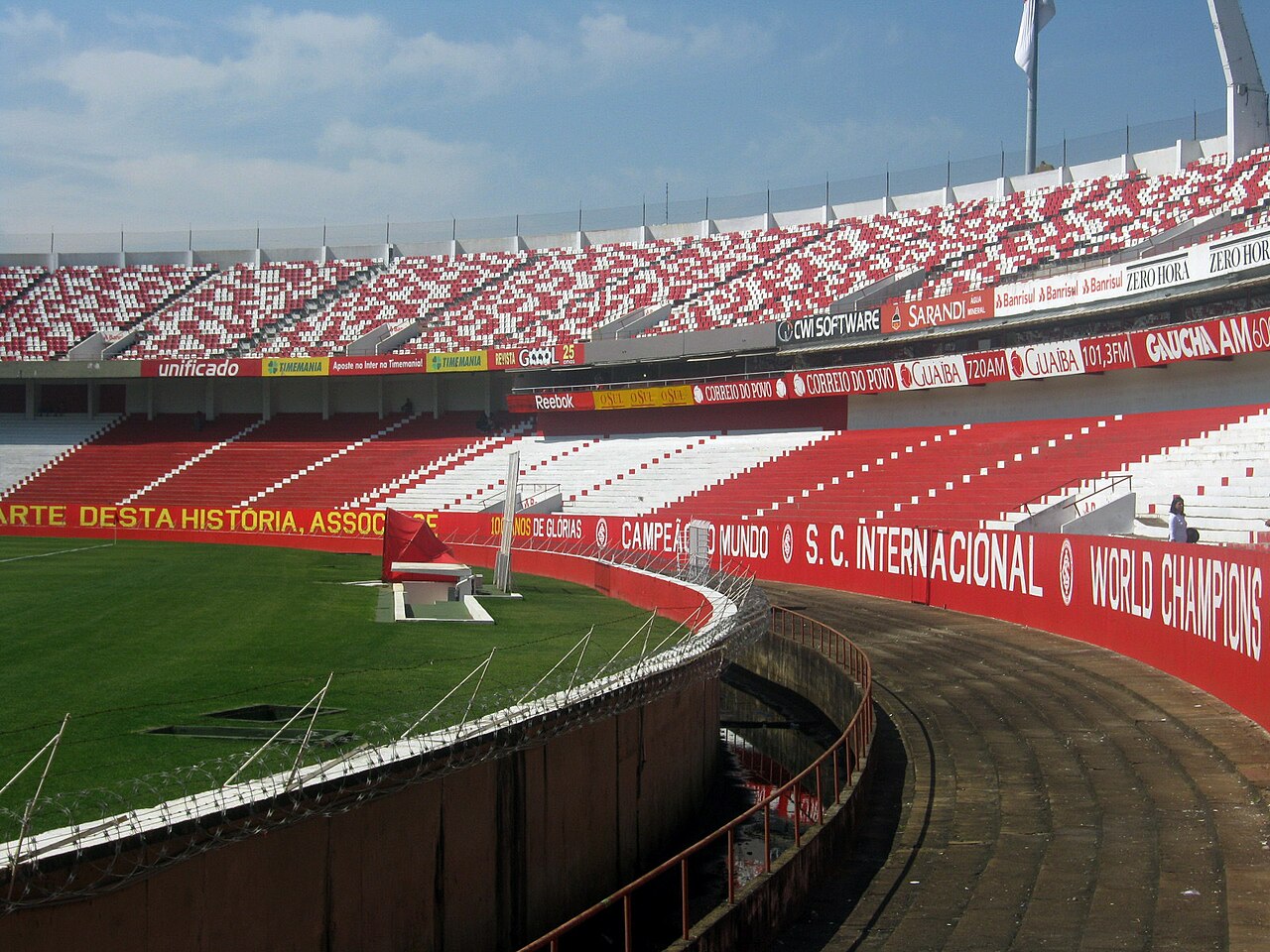 Curved red and white stands of a football stadium with a red S.C. Internacional World Champions banner along the pitch