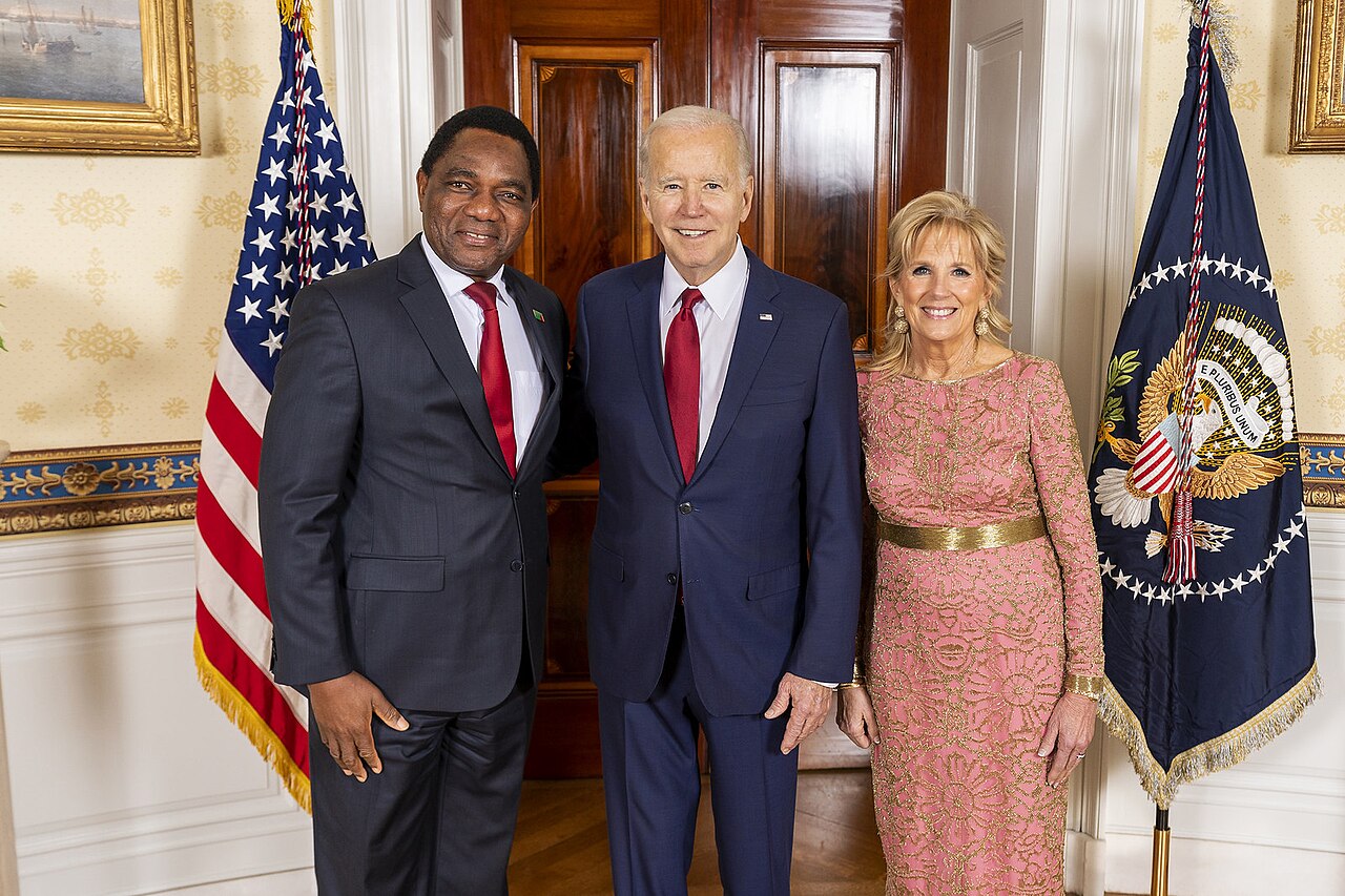 Zambian President Hakainde Hichilema, then US President Joe Biden and First Lady Jill Biden pose together between a US flag and a presidential flag at the White House