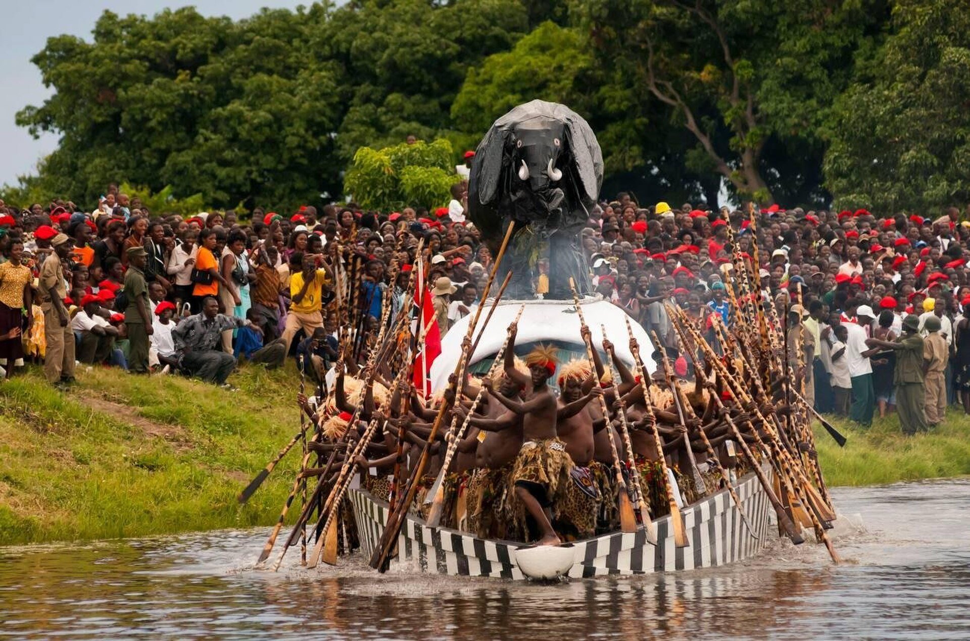 Paddlers in a boat during the Kuomboka ceremony of the Lozi people in Western Province, Zambia, with a large crowd on the riverbank