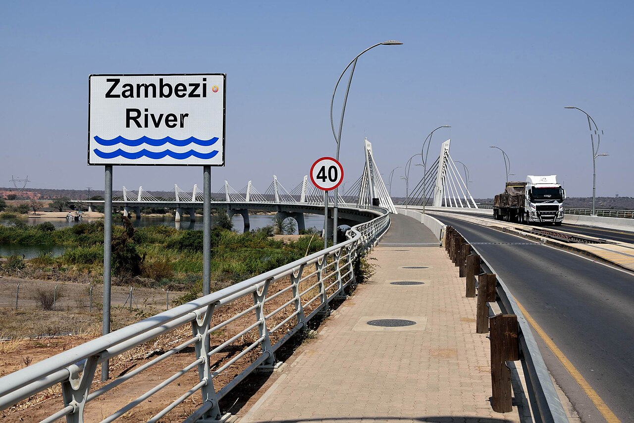 A Zambezi River sign beside the cable-stayed Kazungula Bridge, with a lorry crossing on the road deck