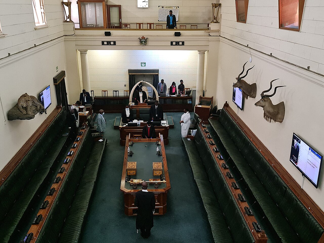 The green-benched chamber of Zimbabwe's National Assembly in Parliament House, Harare, with a mace on the central table and officials standing